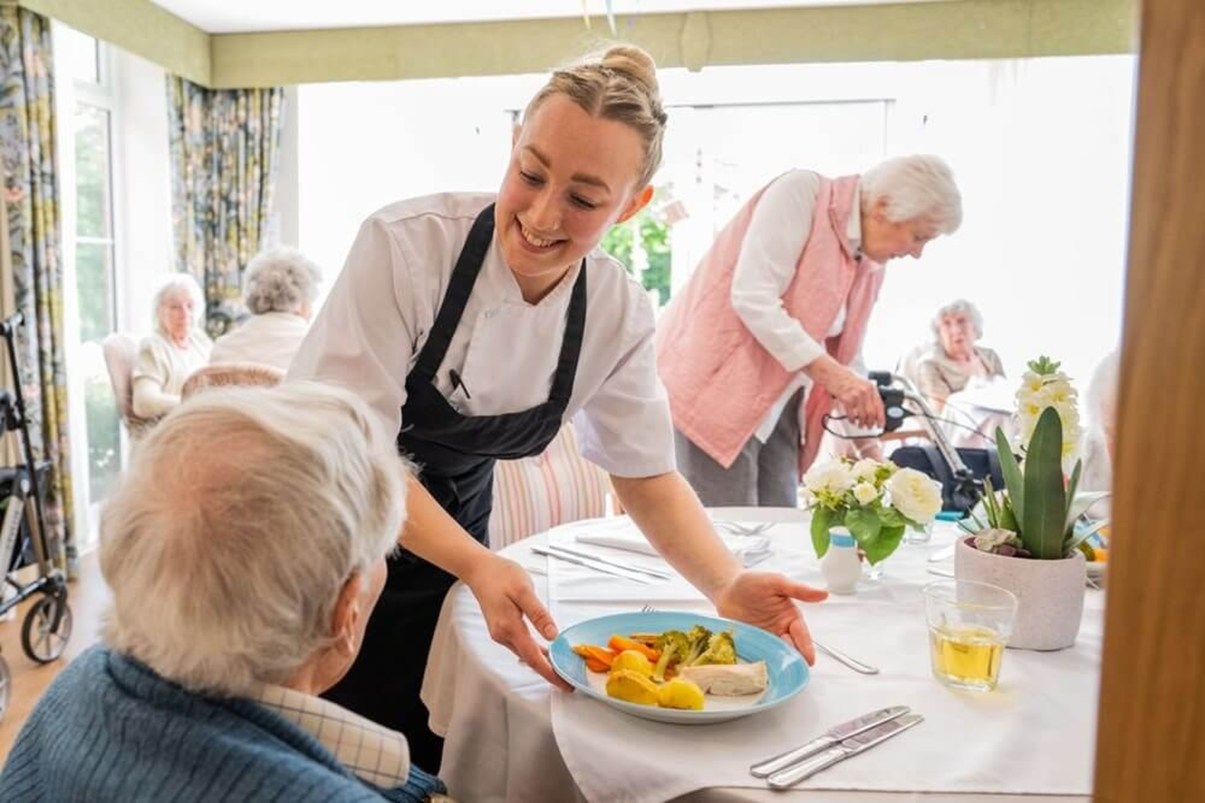 Chef serving a plated meal to an older resident in a care setting